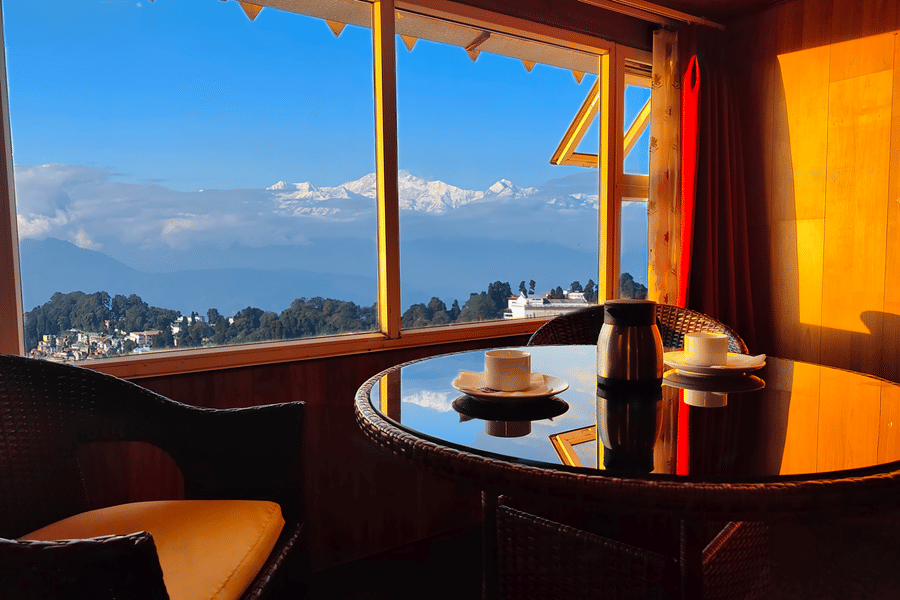 Panoramic window view with seating area and hillside scenery at Mount Thistle Boutique Hotel, Darjeeling.