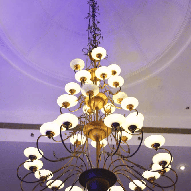 Multi-tiered chandelier at The Bristol Hotel, Gurgaon with rows of white glass shades hanging from a domed ceiling under purple ambient lighting.