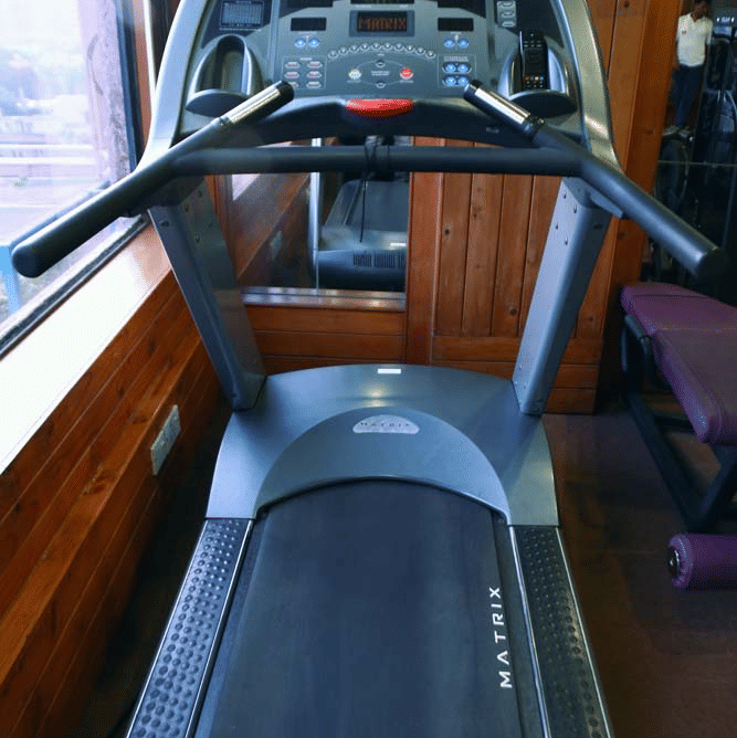 Close-up of a treadmill console in the gym at The Bristol Hotel, Gurgaon with a wall-mounted television above and wood-panelled surroundings.