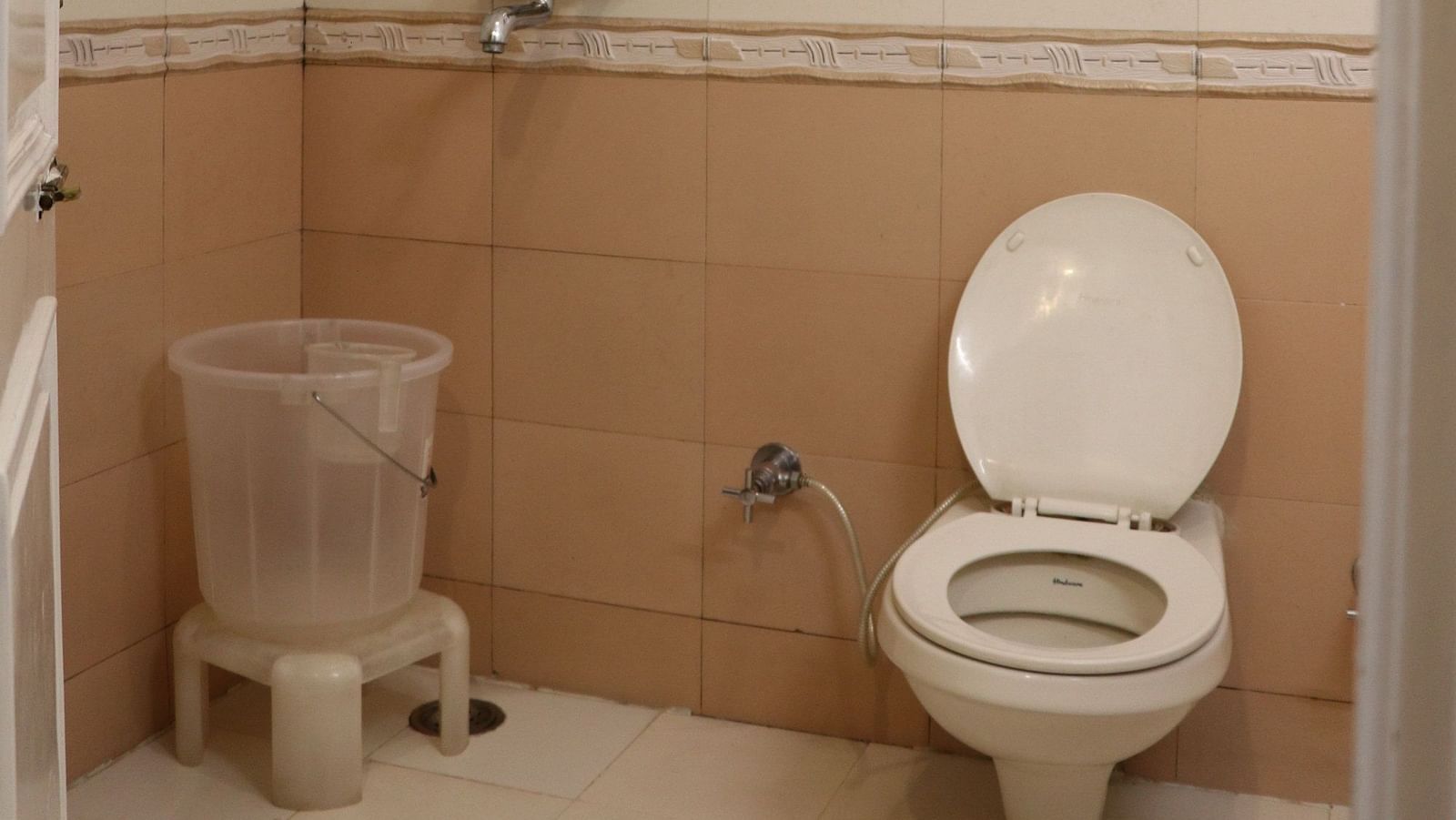 A bathroom with a white toilet, a shower area with a glass panel, and a tiled wall. - Hotel Diamond Plaza, Chandigarh.