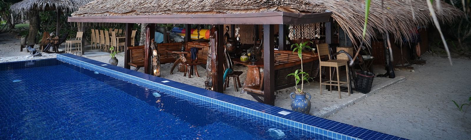 Thatched-roof restaurant by the pool surrounded by palm trees at Flower Island Resort.