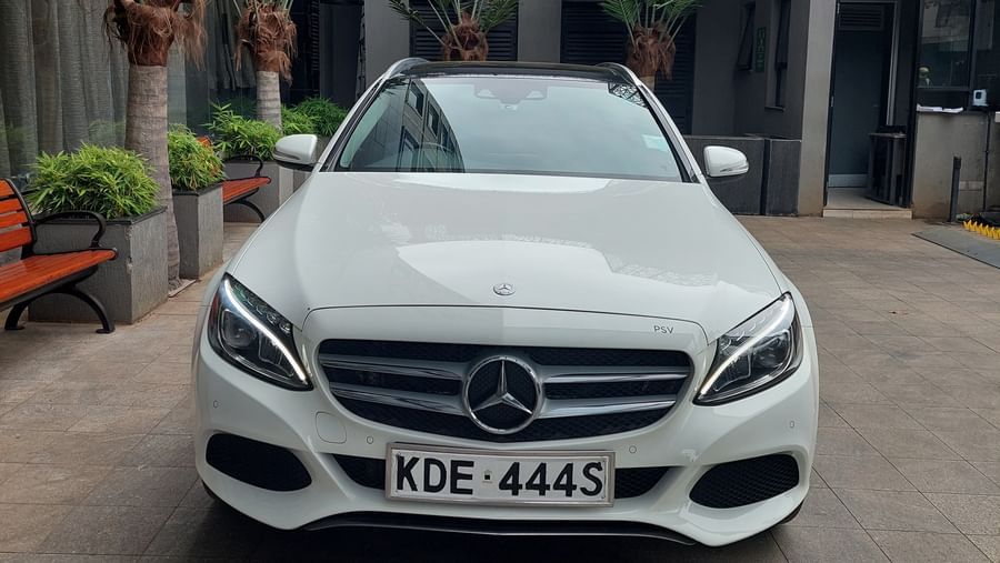 A white Mercedes car parked outdoors in a driveway area with plants in the background.