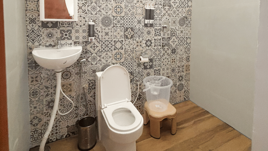 A compact bathroom featuring a ventilation window near the ceiling along with a commode and a wash basin at WOW Naturefull Resorts, Yercaud.