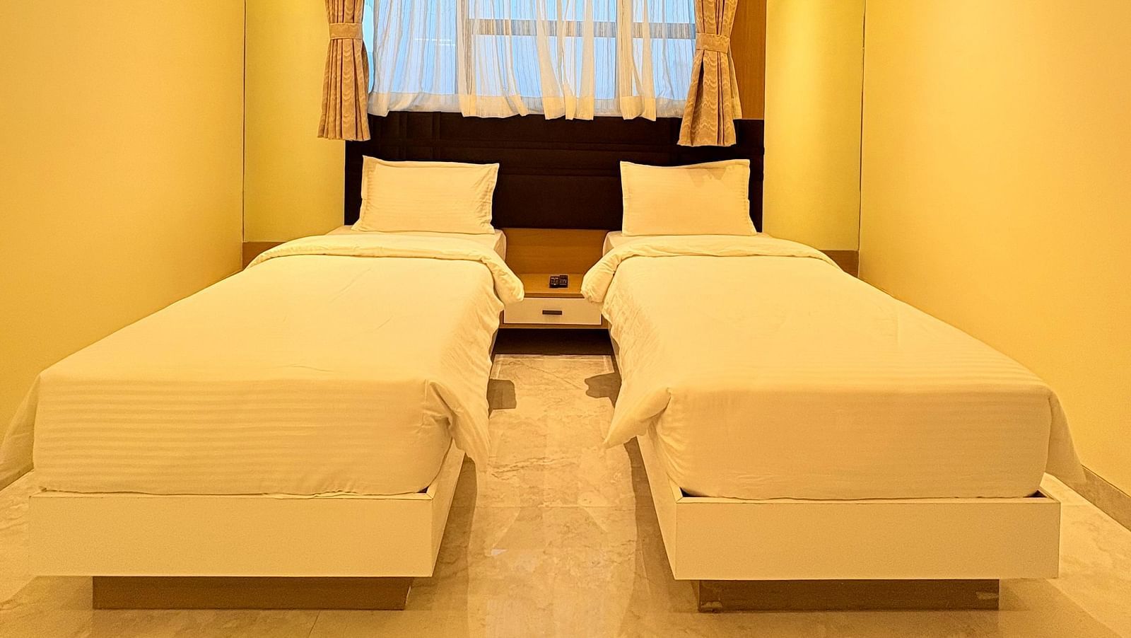 Twin beds in a bedroom with a ceiling fan above at Hotel Mumbai House, Vashi.