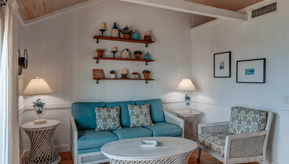 Cozy living room with white wicker furniture, wall-mounted shelves, and wood-style flooring in a seaside cottage | Abaco Inn