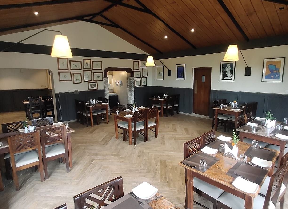 Interior of a restaurant with wooden tables, chairs, and a high ceiling.
