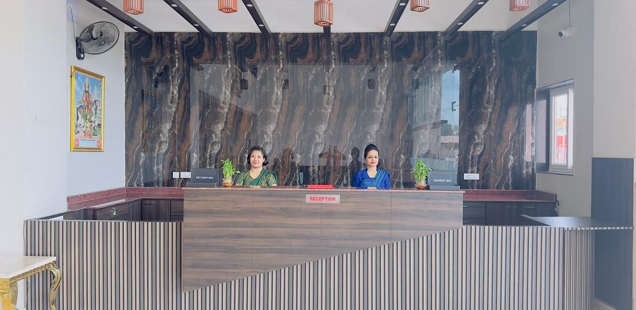 A reception desk with a striped front and wooden beams above is attended by staff - Kankidham Lords Inn