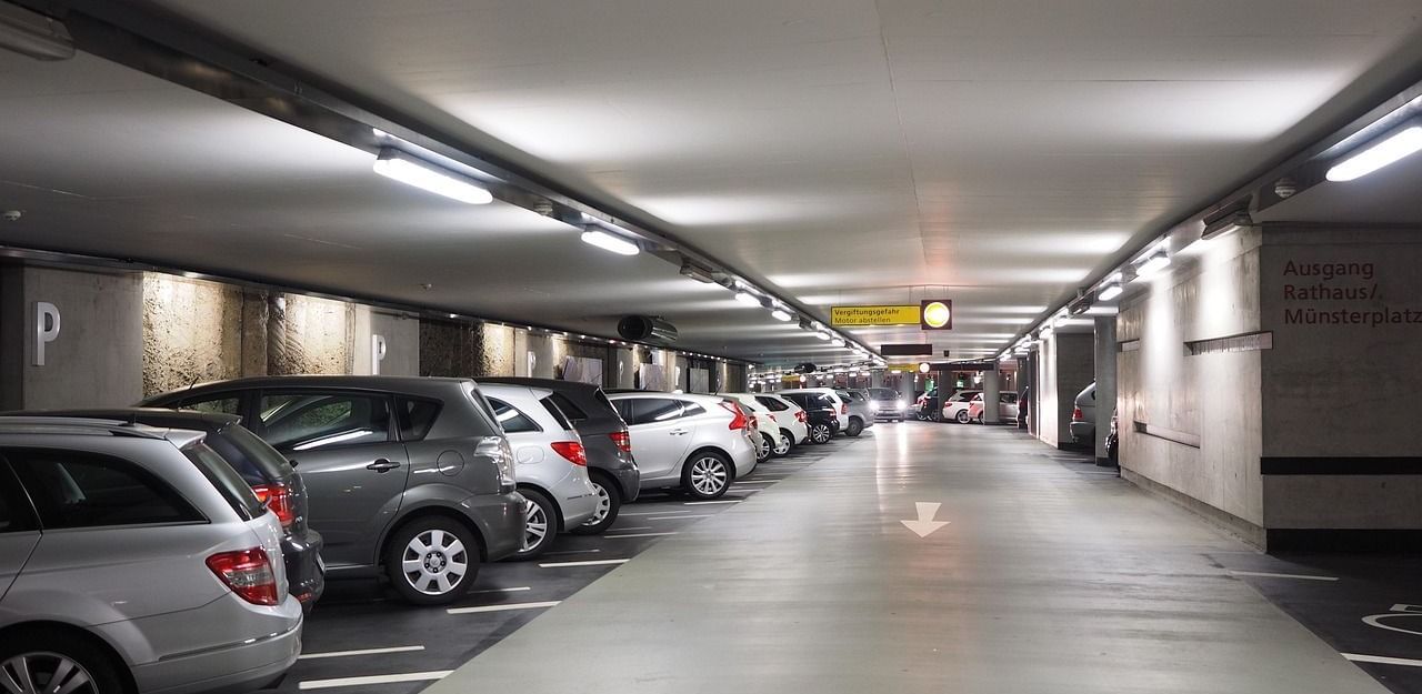 A well-lit underground car park with multiple parked cars on both sides and a central driving lane.