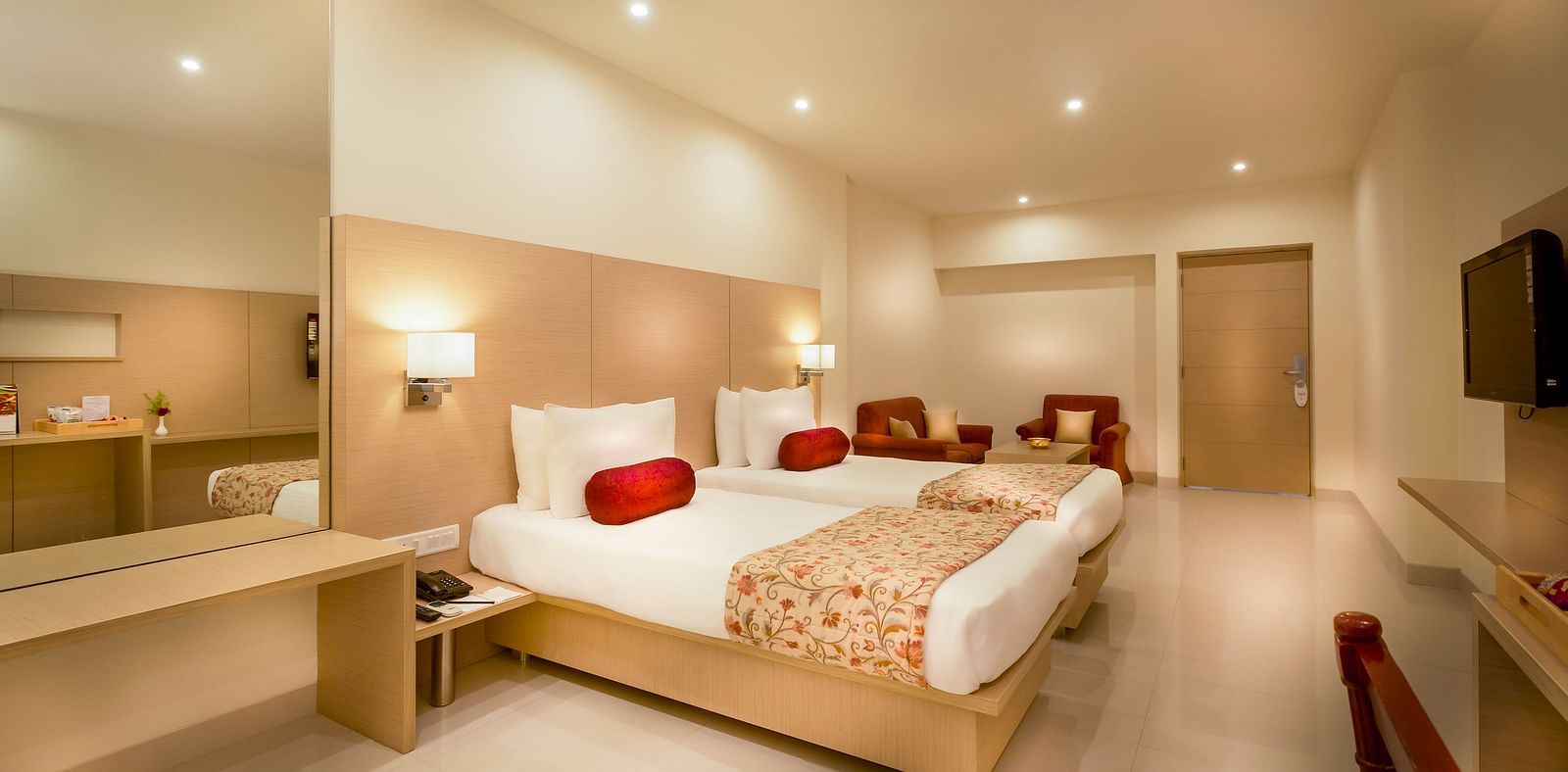 An image of a king size bed with a work desk and TV of a Suite at Regency Tiruttani by GRT Hotels.