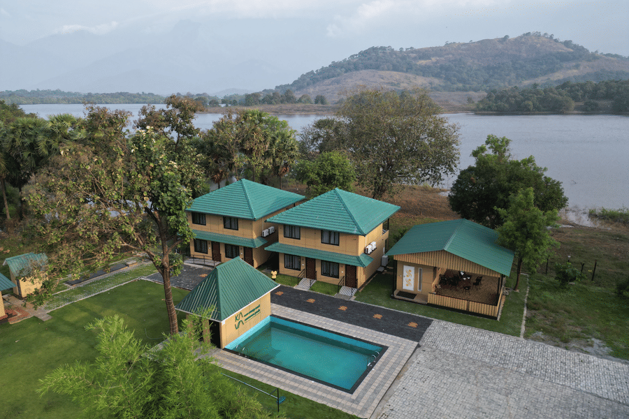 Wide daytime aerial shot of the resort complex situated on the banks of a peaceful lake surrounded by hills - Ibex Resorts, Malampuzha (Kava Eco Camp and Caravan Park)