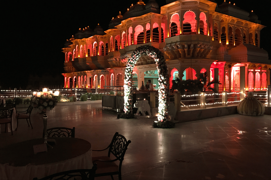 A nighttime outdoor wedding reception at Chunda Palace, Udaipur, featuring a large floral archway entrance and the palace facade glowing with vibrant lighting.