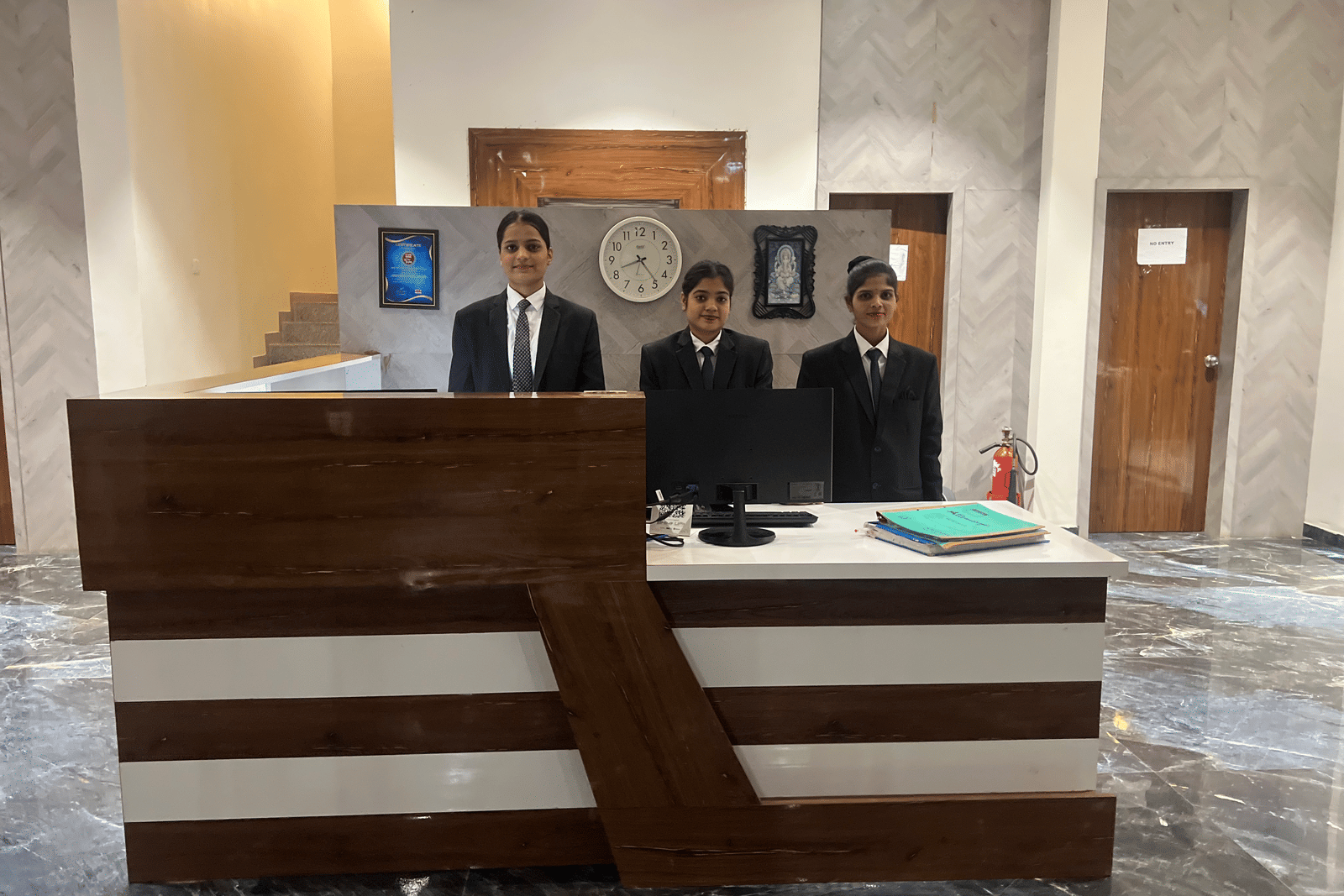 3 people standing at the reception desk of Daksh The Valley Saputara, situated in the lobby area with marble flooring.