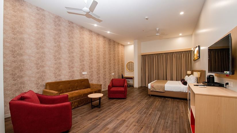 full view of suite room with a set of couch in a corner and a king size bed in another corner - Mastiff Hotel, Ankleshwar