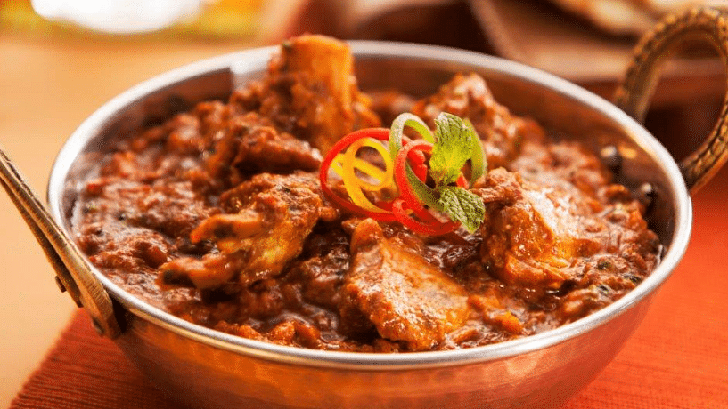 A close view of Laal Maas served in a copper mini kadai, beautifully garnished with vibrant chilies and fresh coriander for an enticing presentation.