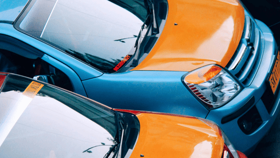 An overhead, tight-crop view of several brightly coloured cars, including orange and blue models, parked closely together.