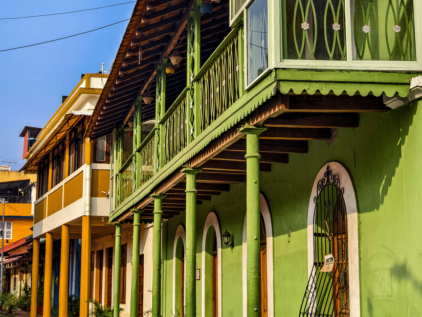 A street-level view of a vibrant green building featuring a wrap-around balcony with glass panels and traditional wooden trim.