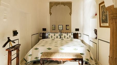 A bright bedroom at Fort Barli, featuring a white arched doorway and a patterned bed, offers a minimalist yet elegant sleeping space.