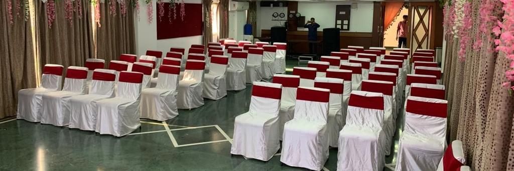 Spacious banquet hall with seating arranged for a seminar or celebration, featuring white chair covers and maroon sashes.