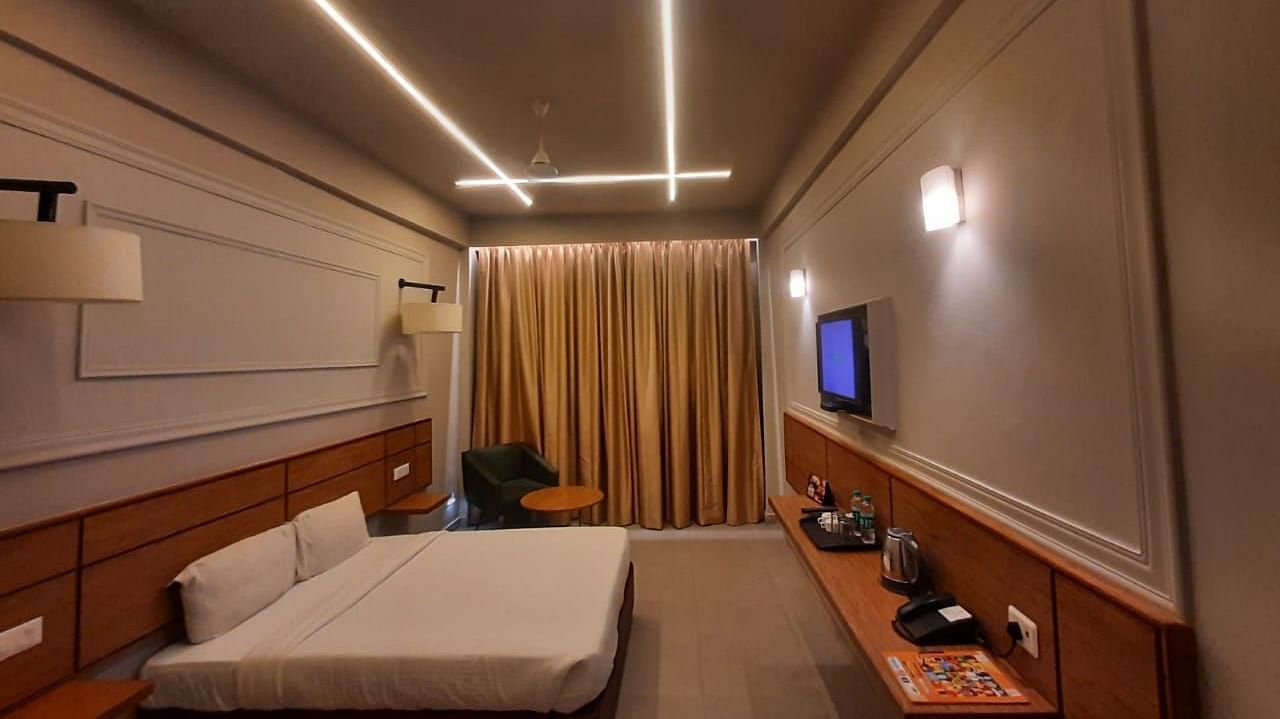 A  side view of a spacious room with a plushy bed and flat screen TV at Max Hotel Prayagraj