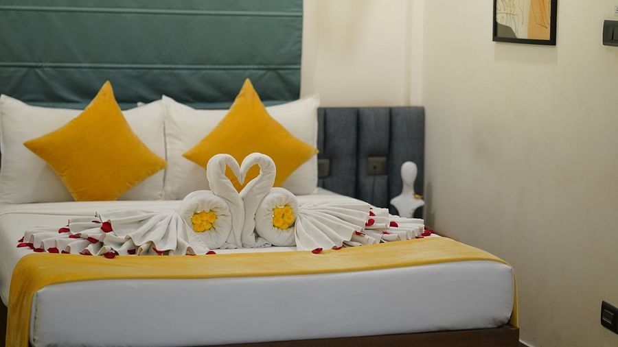 A room with a neatly made double bed adorned with yellow and towels shaped into swans, scattered with rose petals for a welcoming touch at Hotel Kyzen Smartstays – Smart, Reliable, Kyzen
