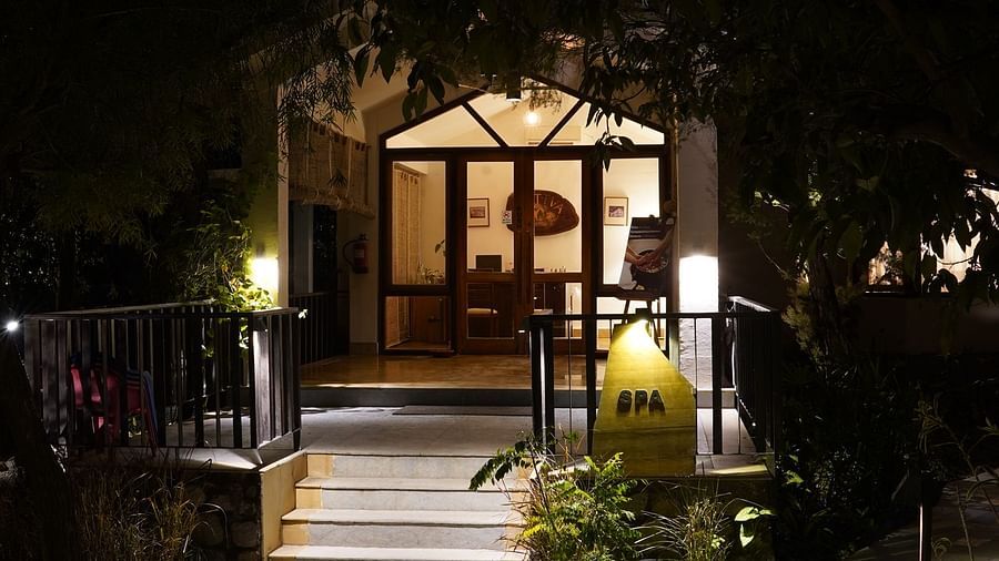Entrance to the spa at Saraca Resort & Spa Corbett with large glass doors with wooden panels and greenery surrounding the building at night
