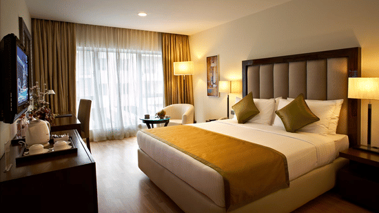 An image of a bedroom featuring double size bed, a flat TV screen, a cabinet, a sofa and centre table, and a few lamps at Adarsh Hamilton