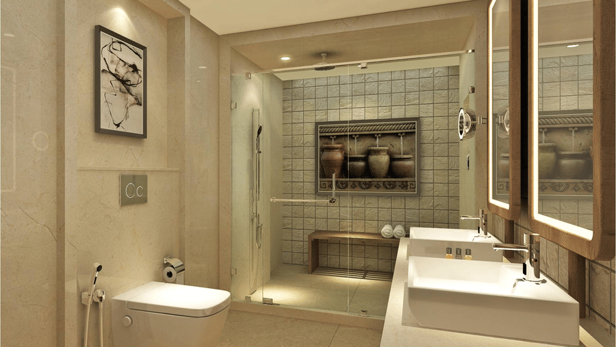 Bathroom inside the Havelock Water Villa featuring a section for shower partitioned with glass walls, mirrors with lights on the wall, wash basin, and a commode. Inside the bathing area there is a photo frame and a bench which has towels.