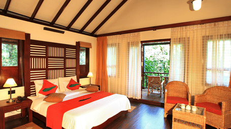 A bed in a room with a balcony with forest views at Vythiri Resort. Wayanad