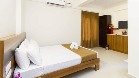 A neatly arranged hotel bedroom with a double bed, dark wood furniture, white walls, and a ceiling fan