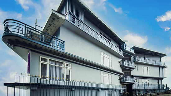Mount Lungta Boutique Hotel & Spa in Darjeeling displaying a long white building with balconies, railings, and scenic hillside surroundings under a bright sky.