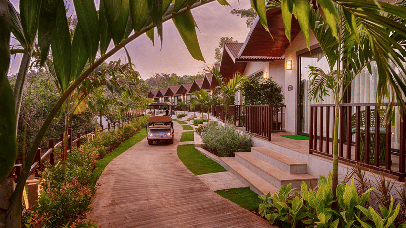 A scenic view of the Premium Cottage at Stone Wood Premier Gokarna, surrounded by lush greenery and a well-paved walkway.
