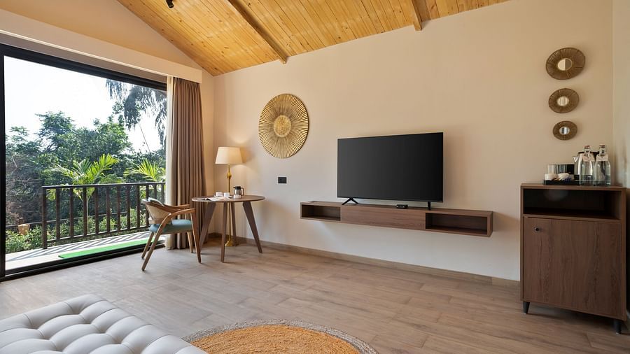  A stylish living space with a TV, wooden interiors, and large windows opening to a green view.