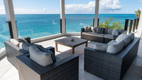 Outdoor seating area with cushioned chairs and a table, overlooking the water at Tamarind Hills Resort and Villas - Antigua.