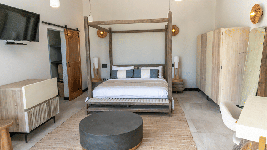 A bedroom with a four-poster bed, a cupboard, a table, a chair, a wall mounted television and furnishings at Tamarind Hills Resort and Villas, Antigua.