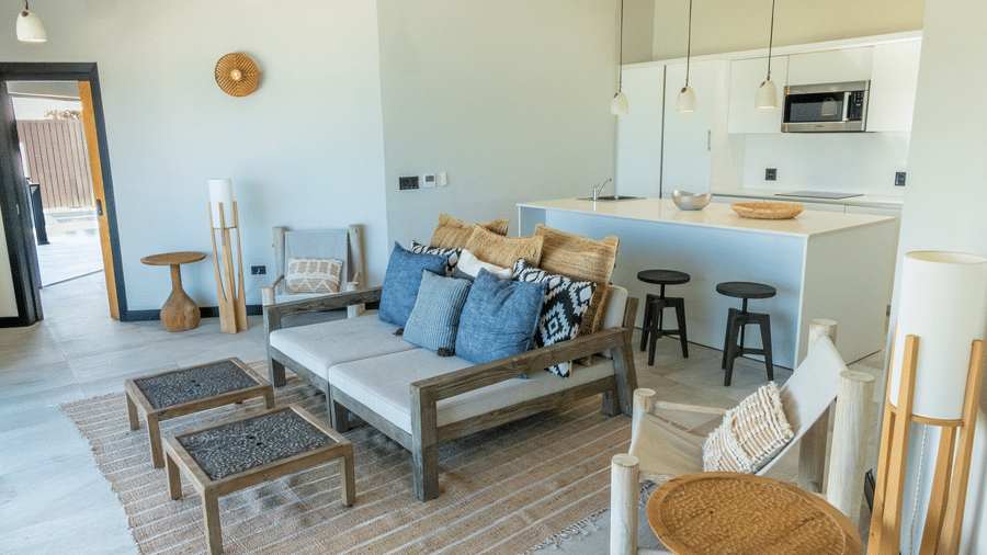 A living room and kitchen with a sofa, two tables, two lounge chairs and a kitchen island at Tamarind Hills Resort and Villas, Antigua.