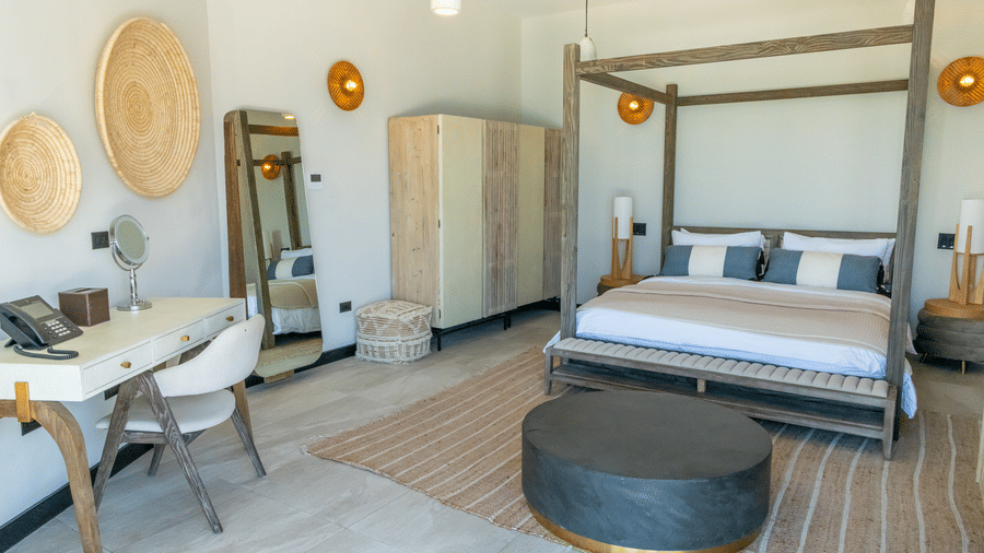 A bedroom with a king size bed, a cabinet, a table, a chair, a cupboard and pendant lights at Tamarind Hills Resort and Villas, Antigua.