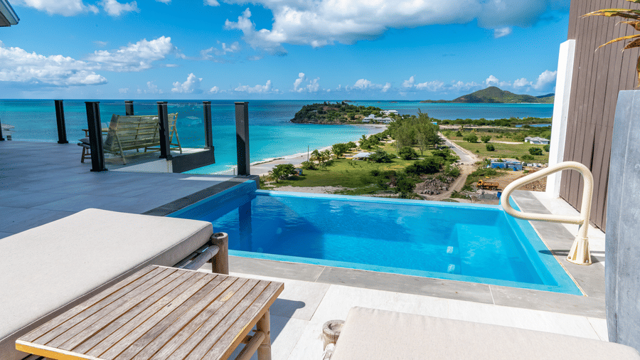An infinity pool with a lounge chair, a table with sea view at Tamarind Hills Resort and Villas, Antigua.