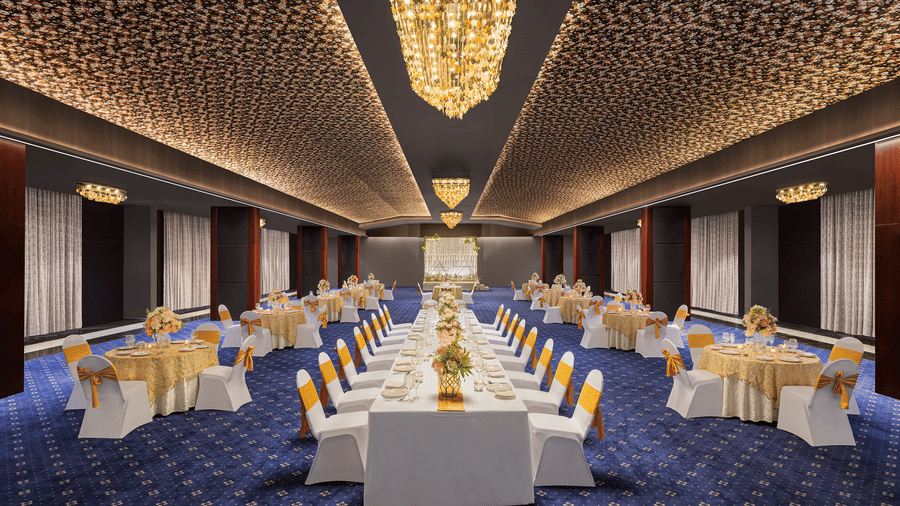 Banquet hall in Indore at Essentia Luxury Hotel with blue carpets, gold-accented seating, and a grand crystal chandelier.