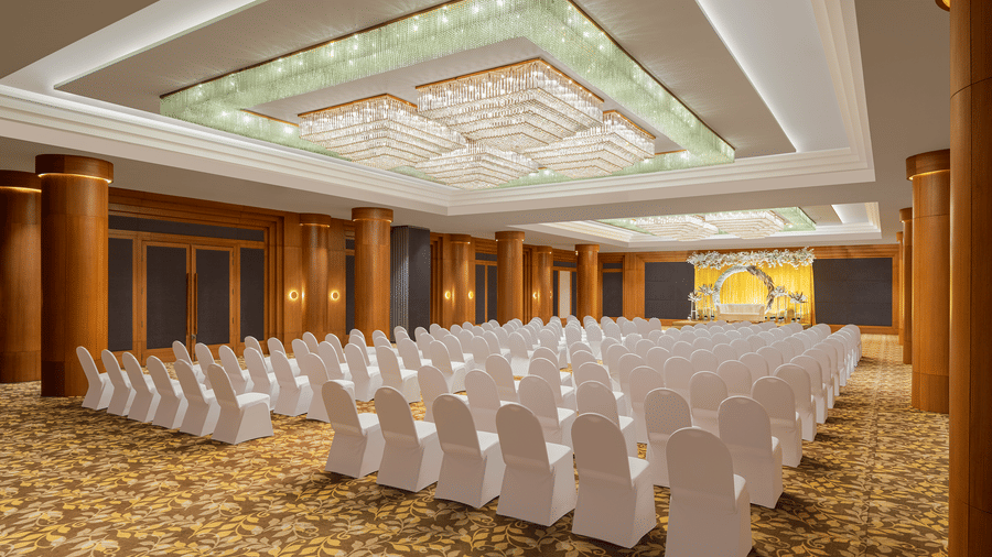 Seating arrangement in Orchid Hall at Essentia Luxury Hotel, Indore, featuring rows of chairs facing the stage under warm lighting on a floor with patterned carpet