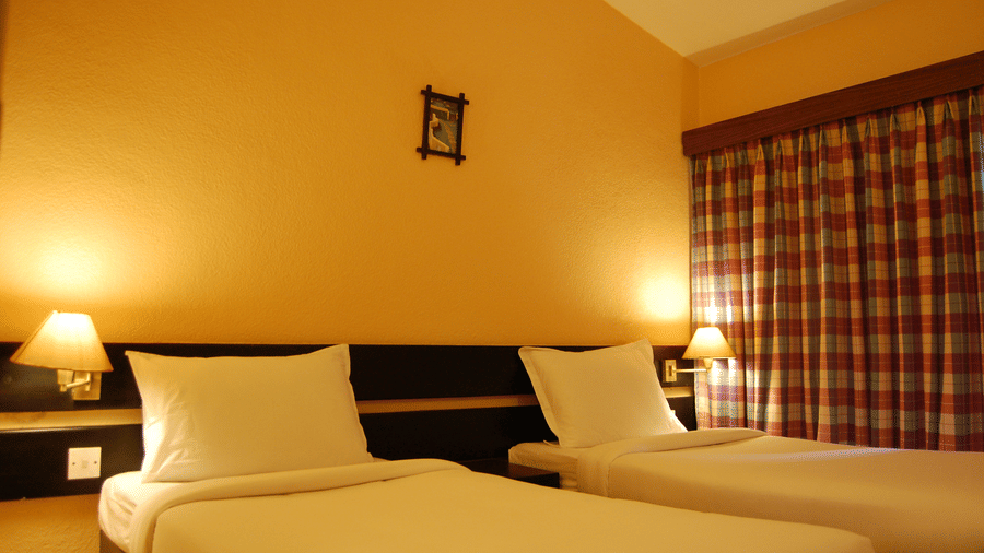 An inviting and restful accommodation at Green Pastures, Kodai, showcasing 2 separate, comfortable single beds with pristine linens, divided by a convenient central headboard structure and bedside lighting.