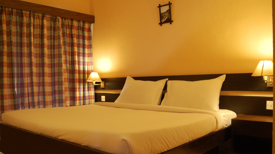 A warmly lit bedroom of Deluxe Cottage at Green Pastures, Kodai, featuring a luxurious bed with crisp linens, bedside tables, and elegant lamps on either side of the headboard