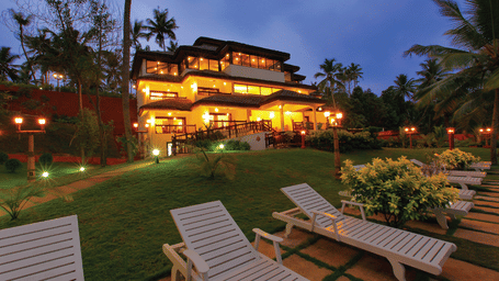 A grand building surrounded by a lush, expansive lawn with three beach beds positioned in the foreground, evoking a serene and inviting atmosphere - Fragrant Nature Kollam