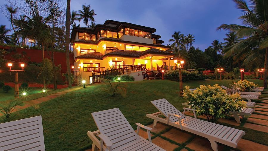 A grand building surrounded by a lush, expansive lawn with three beach beds positioned in the foreground, evoking a serene and inviting atmosphere - Fragrant Nature Kollam