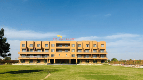 Pride Resort, Jodhpur, with spacious lawn in front and clear sky, showcasing its modern architectural design.