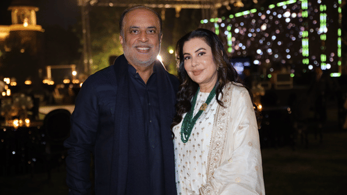 Two guests posing at an outdoor evening event with a glowing backdrop and festive ambience.