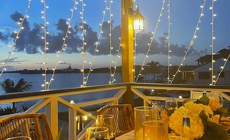 An outdoor dining table set under warm string lights at night, surrounded by tropical flowers and glowing lanterns | Abaco Inn