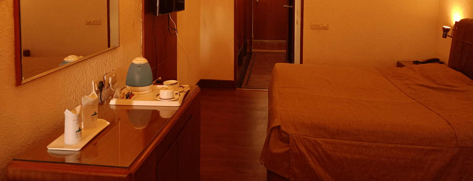 Room interior at Hotel Gold, Panipat with a bed, lamps, desk, and a mirror near the entrance.