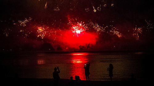 image of bright coloured fireworks bursting on the beach side reflecting on the water surface