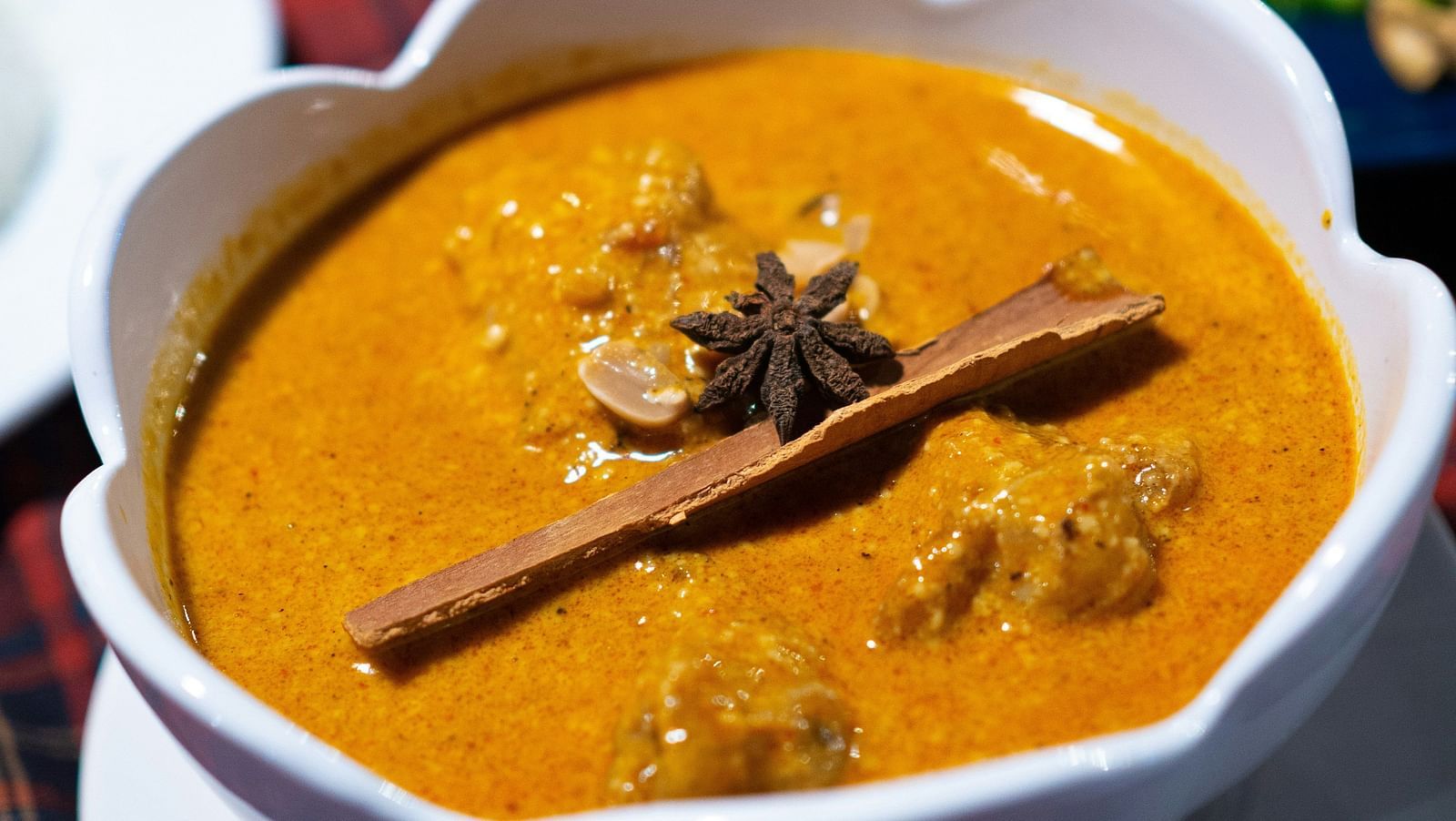 An overview of a curry kept inside a bowl with a star anise and cinnamon stick on top.