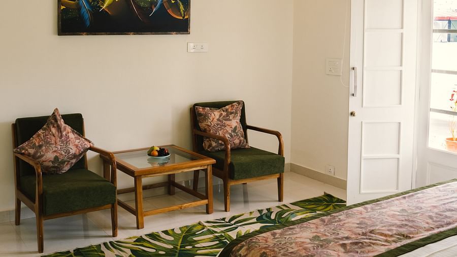 A view from the bedside, with two chairs against the wall, a table between them, and a wall-mounted photo frame above, with a lamp at BluSalzz Villas - The Green Roof, Bhimtal.